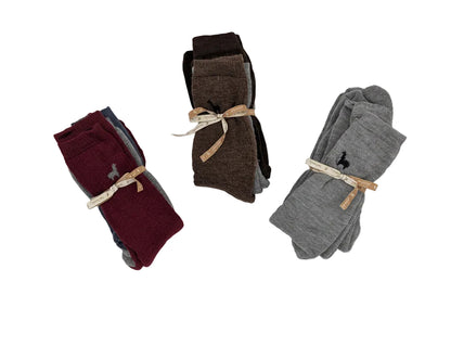 Three folded pairs of socks displayed on a white surface: burgundy and blue on the left, brown and black in the center, and heather gray with a small embroidered polo player on the right. Each pair is tied with a natural twine bow.