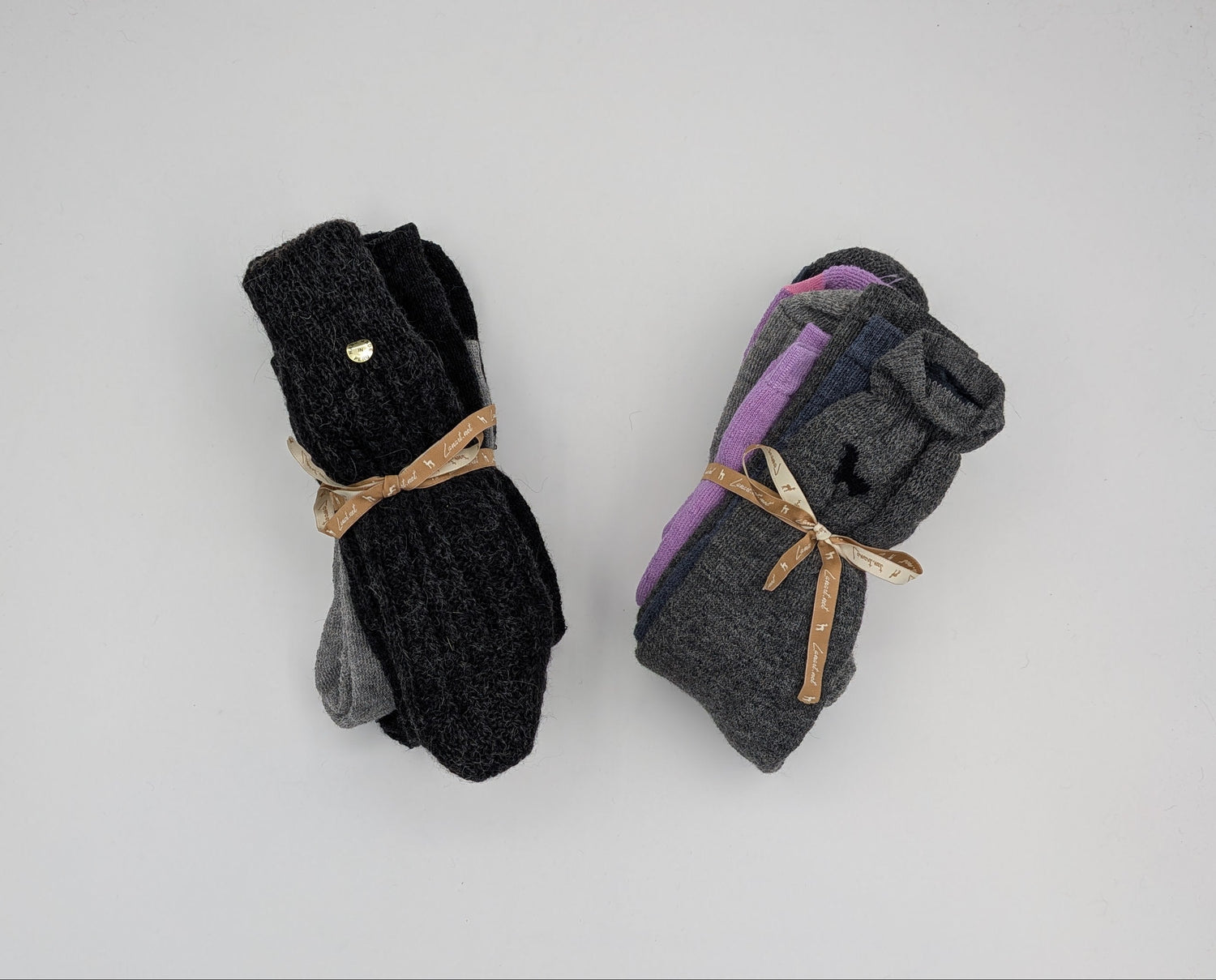 Two pairs of folded socks on a white background. The left pair is black with a small gold button and tied with a tan ribbon.