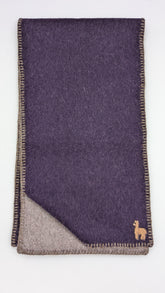 A folded dark purple wool scarf with a beige reverse side, featuring a small embroidered camel logo in the bottom right corner.