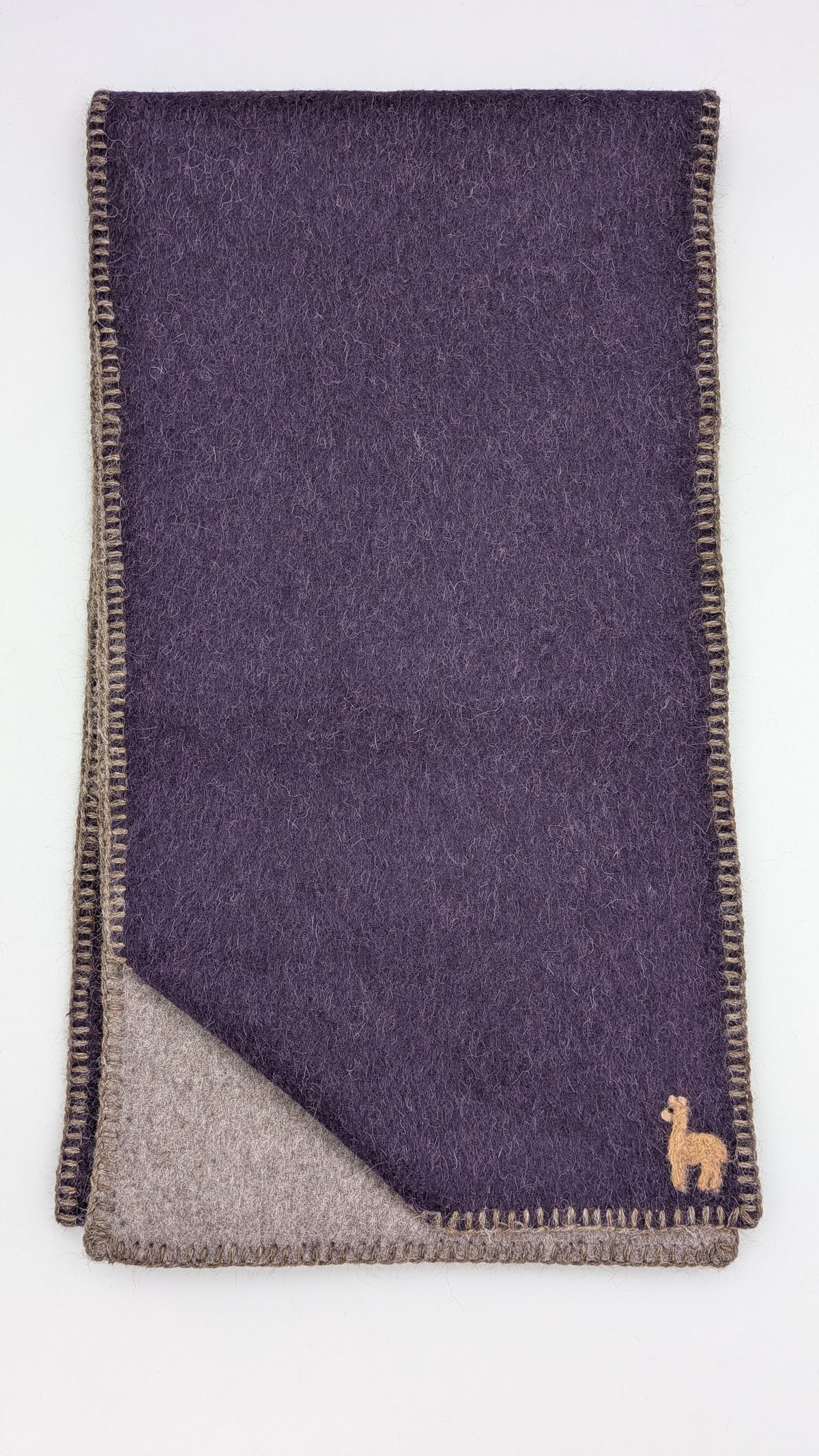 A folded dark purple wool scarf with a beige reverse side, featuring a small embroidered camel logo in the bottom right corner.