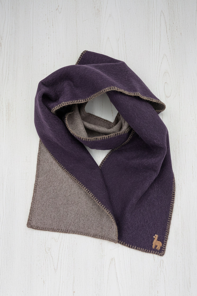 A folded scarf in a deep purple and taupe-brown color-blocked design, displayed on a clean white background. A small embroidered camel logo is visible in the bottom right corner.
