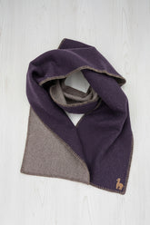 A folded scarf in a deep purple and taupe-brown color-blocked design, displayed on a clean white background. A small embroidered camel logo is visible in the bottom right corner.