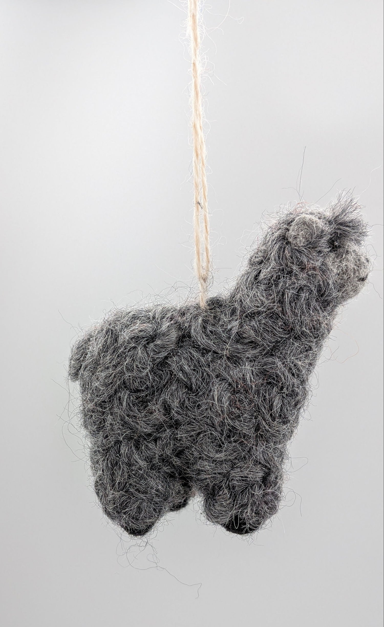 A small gray alpaca-shaped hanging ornament made from curly wool or felt, suspended by a thin string against a plain light background.