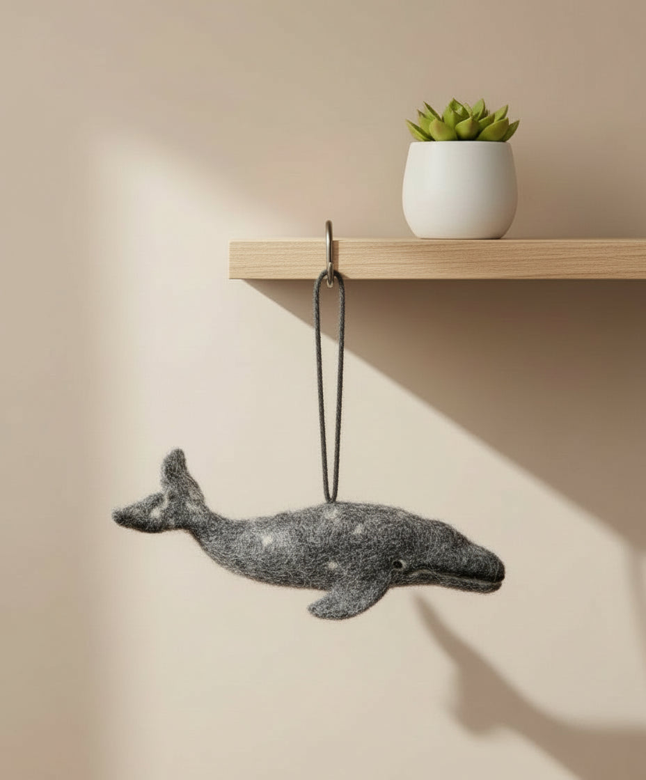 Gray whale ornament hanging on a beige wall with a shelf in the background