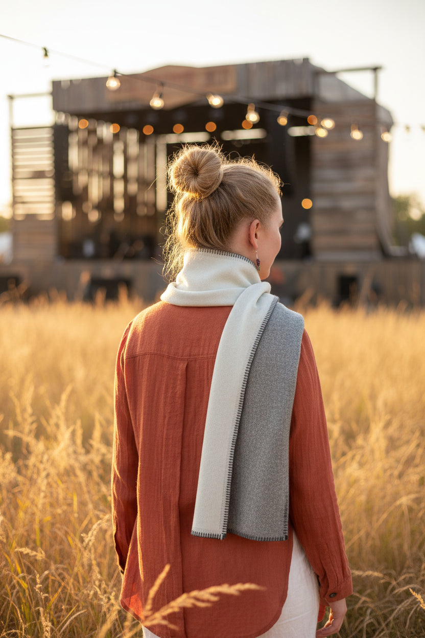 A woman shown from the back wearing a rust-orange linen shirt and a cream and gray alpaca scarf, standing in front of a stage