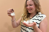 A woman with blonde hair holds a small white fluffy bunny in her hand while wearing a black and white wavy-patterned knit top. She is holding a small white fluffy bunny on a black hair tie in her other hand.