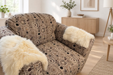 A close-up of a patterned loveseat or sofa in a real living room, with two cream alpaca-fur throw pillows resting on the seat and armrests. 