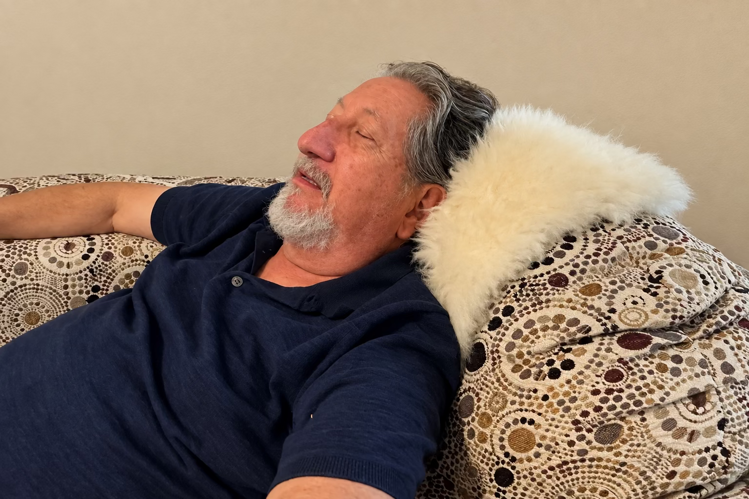 A man reclining on a sofa with a white alpaca fur pad in a living room setting.