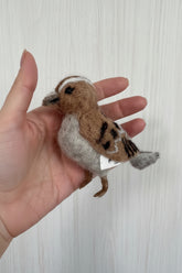 A hand-held felted wool bird figurine with brown, white, and black detailing, shown against a plain light background.