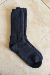 A pair of dark charcoal gray knit socks laid flat on a brown cardboard box, with a gray stone-tile floor visible in the background.