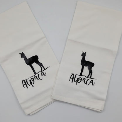Two white towels with black llama graphics and text on a light gray background