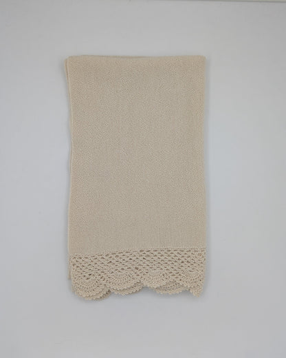 A beige alpaca shawl with a decorative crocheted lace hem, hanging on a white wall.
