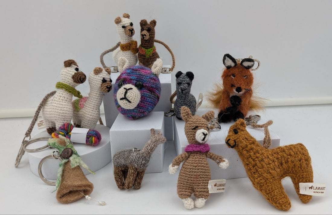 A collection of handmade crocheted animal toys displayed on white blocks against a white background. The set includes a brown llama, a gray giraffe, a brown fox, a gray cat, a white dog, a brown bear, a purple and blue ball, and other small stuffed animals.