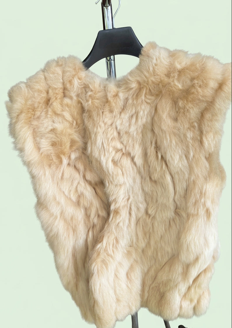 A fluffy fur vest in a light beige color, displayed on a black hanger mounted on a metal stand.