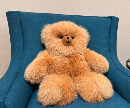 Large teddy bear sitting on a blue armchair in a room with a plant and small table.