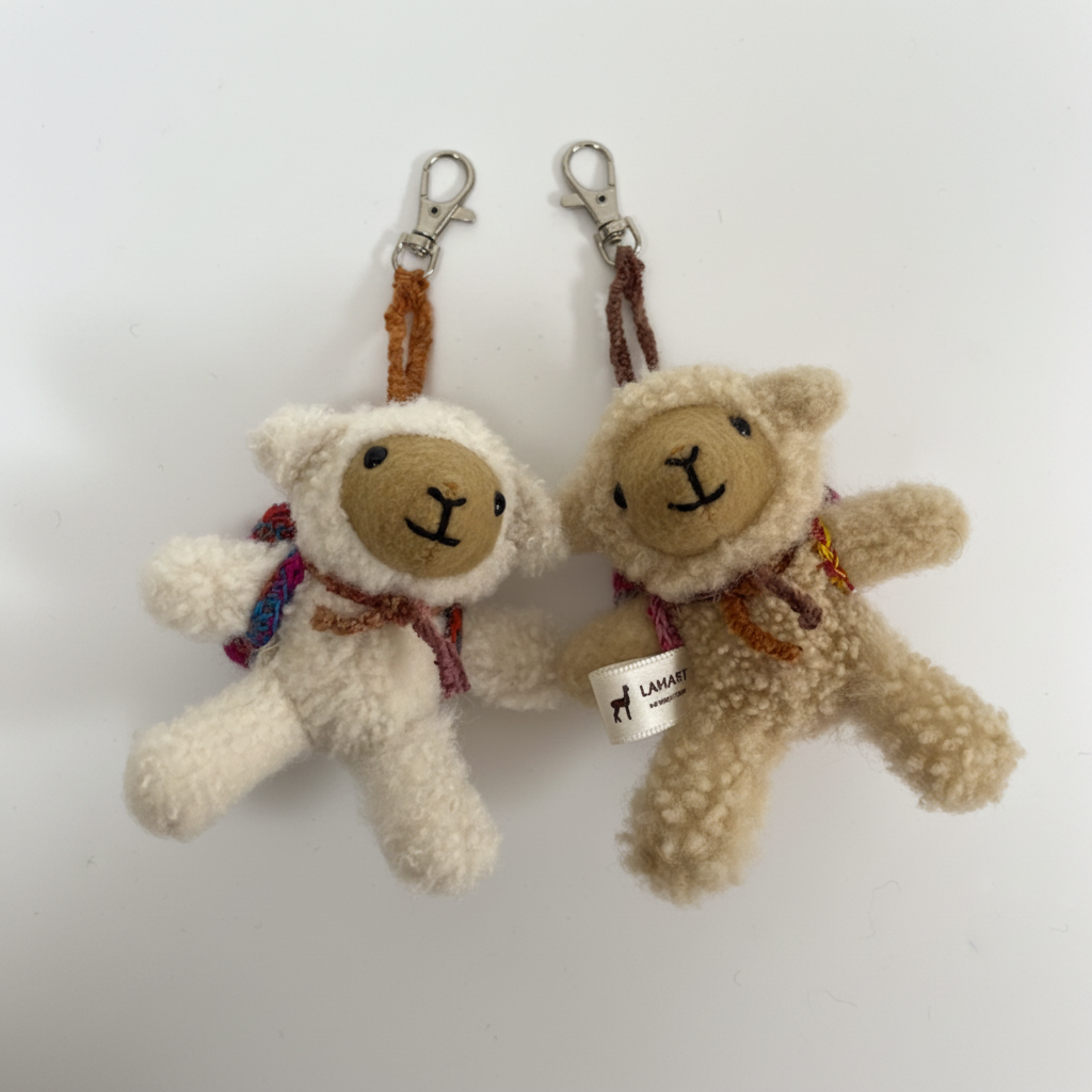 Two small plush teddy bear keychains on a plain white background. One is cream-colored with a tan face and a purple patterned scarf, attached to a brown strap and silver clasp.