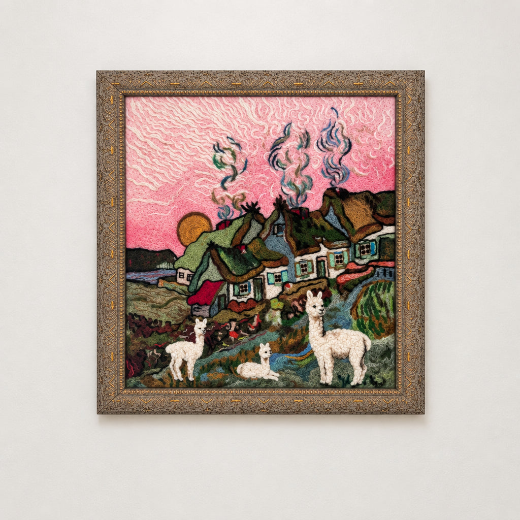 A framed felted art piece depicting a village scene with alpacas in the foreground, hanging on a plain white wall.
