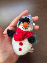 A needle-felted alpaca fiber snowman sculpture with a red hat and carrot nose, in a hand.