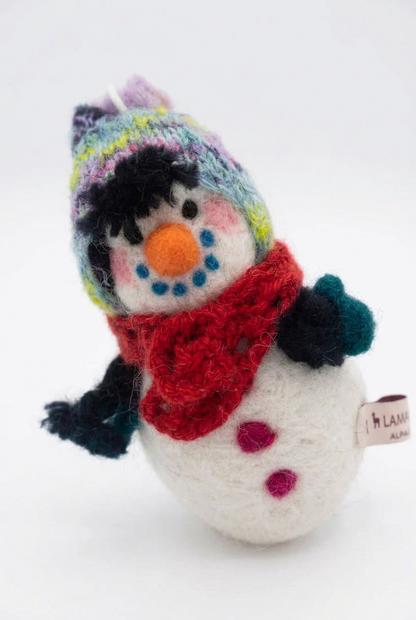 A needle-felted alpaca fiber snowman sculpture with a red hat and carrot nose, leaning against a white background.