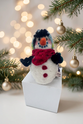 A needle-felted alpaca fiber snowman sculpture with a red hat and carrot nose, against holiday decorations.