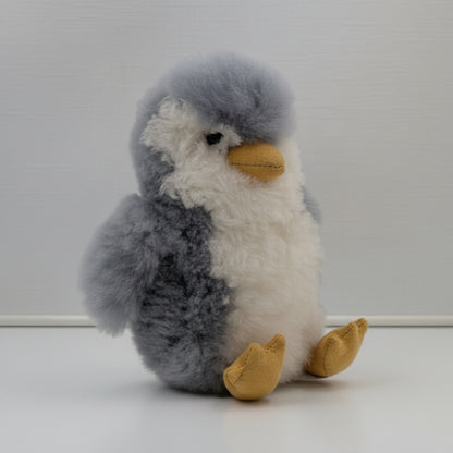 Stuffed alpaca fur penguin with gray, white, and yellow colors on a plain background