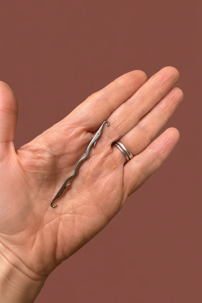 A close-up of a hand holding a small, wavy silver metal needle
