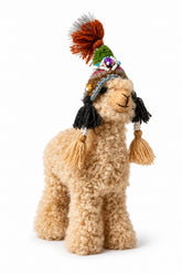 Plushie alpaca wearing a decorative chullo hat with tassels on a plain background