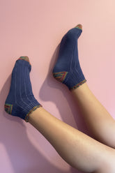 A pair of blue ankle socks with multicolor striped toe and cuff details, shown on a person&