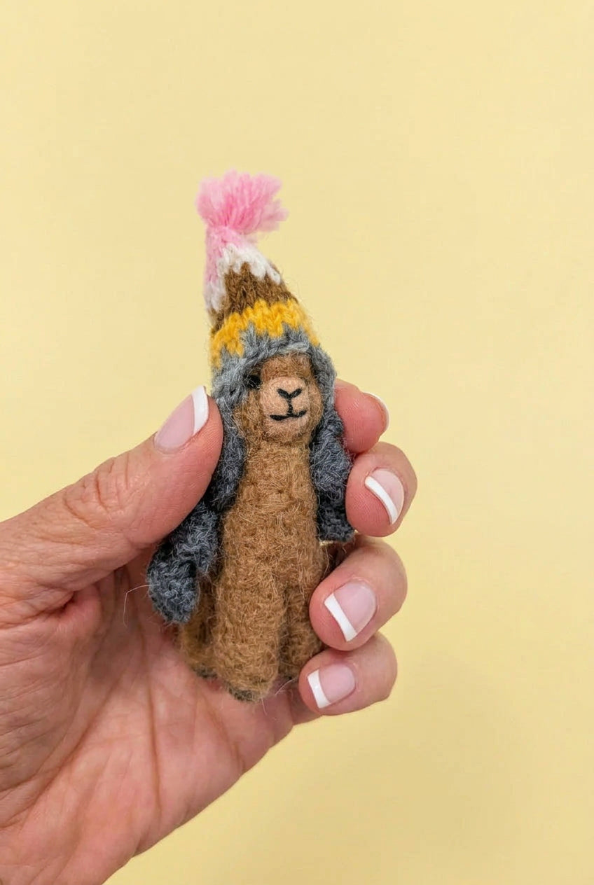 A small handmade tiny alpaca doll wearing a striped knit hat with a pink pom-pom, held in a person&