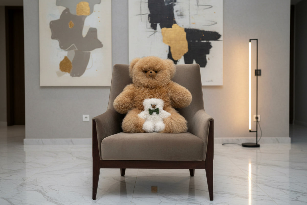 Honey teddy bear with a small pearl teddy bear sitting on a gray armchair in a modern room with abstract art on the wall.